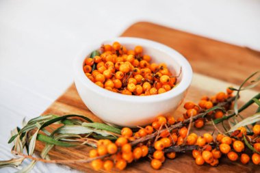 Taze toplanmış deniz dikenli üzümler beyaz tabakta ve kesme tahtasındaki deniz dikenli dallar..