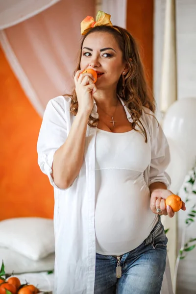 Pregnant woman eating tangerines in her bedroom at home. Healthy eating during pregnancy concept.