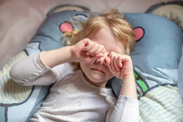 Stock image A young girl is lying on a bed, her hands covering her face. She appears lost in thought or contemplation, with a peaceful expression on her face.