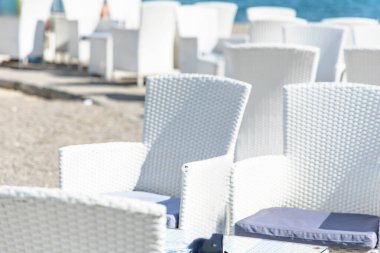 Hırvatistan 'ın Opatija kentindeki kumlu bir plaja bakan bir terasta bir sıra beyaz hasır sandalye oturuyor. Sandalyeler sıraya dizilmiş, bazıları denize bakıyor, diğerleri de verandaya bakıyor.. 