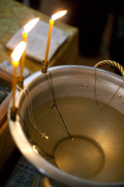 İçi su dolu gümüş bir leğen ve muhtemelen vaftiz töreninin bir parçası olan üç mum parlak bir şekilde yanıyor..