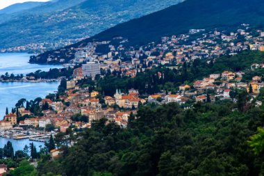 Hırvatistan 'ın Opatija kentinin Adriyatik Denizi' ne bakan bir yamaçtan panoramik manzarası. Şehir, yemyeşil yemyeşil bir arazinin ortasında uzanan körfezin mavi suları....
