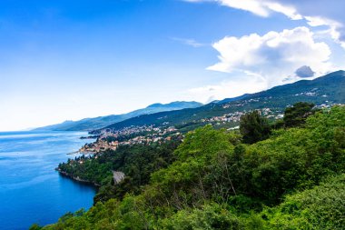 Hırvatistan 'ın Opatija kıyı şeridi manzaralı, yemyeşil ormanlar ve uzakta uzanan mavi Adriyatik Denizi. Beyaz bulutlar açık mavi gökyüzünde sürükleniyor.