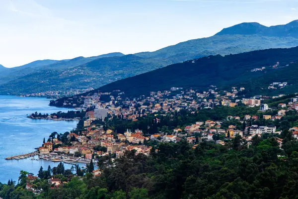 Hırvatistan 'daki Opatija kıyı şeridinin panoramik bir görüntüsü. Görüntü, Adriyatik Denizi ile orman tepeleri arasında yuva yapmış, pitoresk bir limanı ve büyüleyici binaları olan kasabayı yakalıyor..