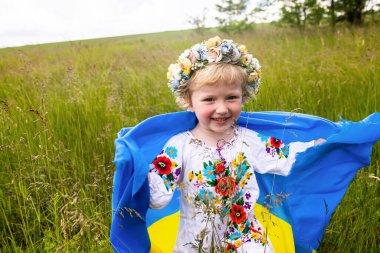 Sarı mavi Ukrayna bayrağı ezilmiş buğday tarlasında koşan kızın ellerinde. Ukrayna bayrağı taşıyan mutlu çocuk. Bağımsızlık Günü. Bayrak Günü. Anayasa Günü