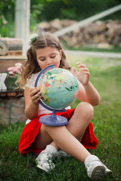 stock image A young girl sits in the grass, holding a small globe in her hands.. Back to School concept