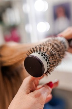 Bir kuaför sarı saçlı yuvarlak bir fırça tutar..