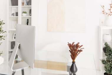 Cam masası, bilgisayarı ve kurumuş çiçekleri olan minimalist bir ev ofisi..