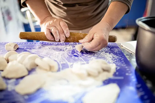 stock image A person shapes a piece of dough for dumplings on a blue cutting mat.