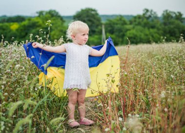 Neşeli bir çocuk Ukrayna bayrağını canlı bir tarlada sergiliyor. Ukrayna 'nın Bağımsızlık Günü' nü kır çiçeklerinin ortasında kutluyor..
