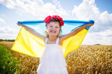 Neşeli genç bir kız, Ukrayna 'nın Bağımsızlık Günü' nü büyük bir buğday tarlasında ulusal bayrak sallayarak kutluyor. Canlı bir çiçek tacıyla süslenmiş beyaz bir elbise giyiyor. Parlayan gülüşü özgürlüğün ruhunu yansıtıyor. Mavi ve sarı.