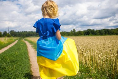 Beyazlar içindeki genç bir kız, Ukrayna 'nın ulusal gururunu sembolize eden mavi ve sarı bir bayrak taşıyor. Altın buğdayın ortasında duruyor, Bağımsızlık Günü 'nü kutluyor, pofuduk bulutlarla süslenmiş açık mavi bir gökyüzünün altında..  