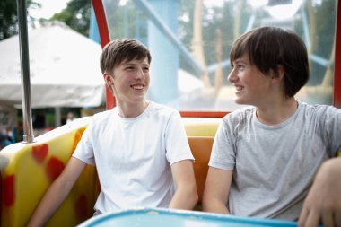 Renkli bir lunapark gezisinde yan yana oturan iki genç çocuk güneşli bir öğleden sonra birlikte eğlenirken mutlu bir şekilde gülüyor ve sohbet ediyorlar..