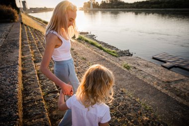 Hırvatistan 'ın Osijek kentindeki Drava Nehri kıyısında, güneş batarken ve suyun üzerinde sıcak bir parıltı saçarken, bir kadın ve bir çocuk huzurlu bir yaz akşamının tadını çıkarıyorlar..