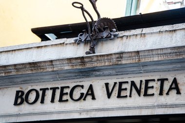 Venedik, İtalya, 17 Ağustos 2024: Mağaza vitrininde Bottega Veneta adı belirgin bir şekilde sergileniyor, parlak gün ışığı altında canlı bir şehirde mimari ayrıntılarla vurgulanıyor.