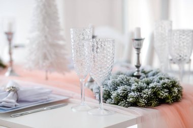 Güzelce düzenlenmiş bir tatil masasında kristal bardaklar, gümüş şamdanlar ve buzlu yeşillik manzarası yer alıyor. Aydınlık oda kutlamanın atmosferini arttırır..
