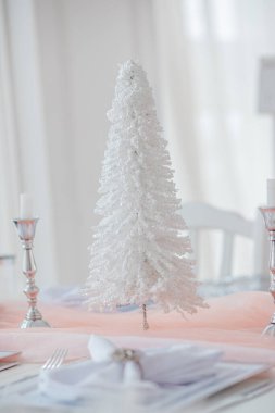 A beautifully arranged table showcases a delicate white tree, candle holders, and neatly folded napkins. Soft lighting enhances the festive atmosphere, perfect for seasonal celebrations. clipart