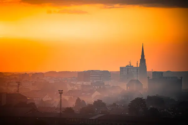 Hırvatistan 'ın Osijek kentinde güneş şehrin silueti ve bir kilise kulesinin silueti ardında batarken, güzel bir günbatımı gökyüzünü resmediyor..