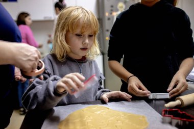 Küçük çocuklar bir yemek pişirme seansına katılıyor, hamur yoğuruyor ve neşeli şekiller yaratmak için kurabiye keskisi kullanıyor. Noel Sanatı