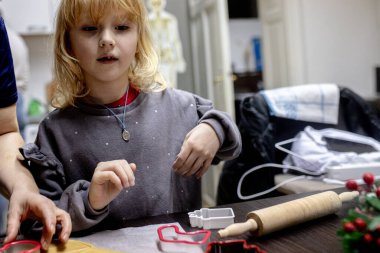Heyecanlı ve nişanlı olan küçük bir çocuk aktif olarak kurabiye pişirmeye katılıyor. Konforlu mutfak ortamında, şenlikli bir ortam yaratmak gibi pişirme aletleri kullanılıyor. Noel Sanatı