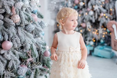 Beyaz kız Noel ağacını süslüyor. Evdeki Noel ağacının yanında güzel elbiseli bir çocuk.