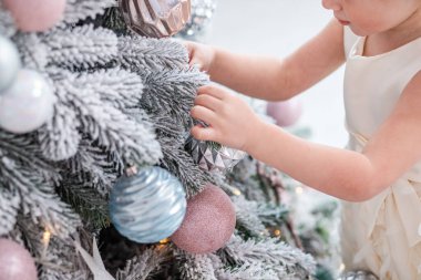 Şık, modern bir Noel ağacının süslerini düzenleyen, tatil elbisesi giymiş küçük bir kızın festival sahnesi..