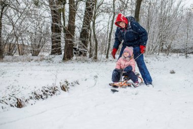 İki çocuk karla kaplı bir tepeden kayıyor, etrafları uzun ağaçlarla çevrili. Sıcak kışlık giysiler içinde serin bir öğleden sonra neşeyle gülüyorlar..