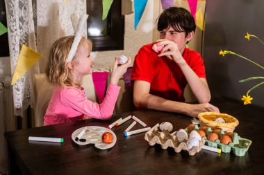 A festive atmosphere as siblings enjoy crafting and painting Easter eggs, capturing the spirit of the holiday. clipart