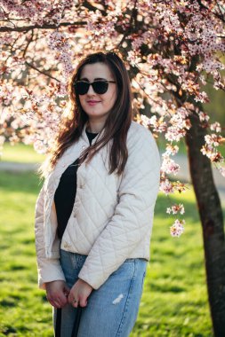 Gün batımında bir parkta pembe çiçeklerin ortasında duran bir kadın..