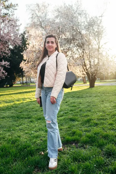 Gün batımında parkta yürüyen kadın, çiçek açan ağaçların güzelliğinin tadını çıkarıyor..