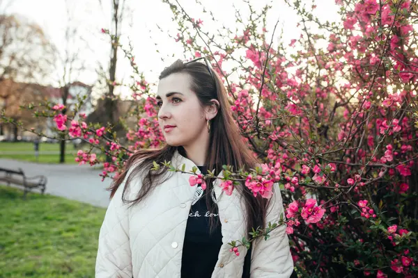 Gün batımında bir parkta pembe çiçeklerin ortasında duran bir kadın..