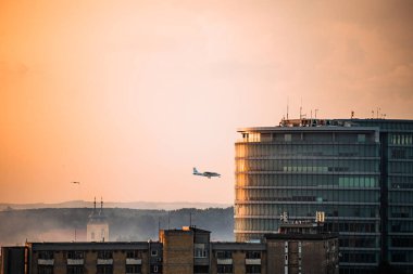 Gündoğumunda Osijek 'teki modern ofis binasından geçen uçak ve arka planda sivrisinek kontrol sisi, şehir sağlık önlemleri.