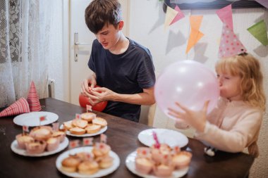 İki kardeş, renkli süslemeler, kapkek tabakları ve neşe ve neşe dolu neşeli bir atmosferle çevrili evde doğum günü kutlamalarının tadını çıkarıyorlar..