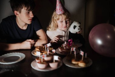 Kardeş ikilisi lezzetli kekler, renkli parti şapkaları ve neşeli anlarla dolu bir doğum günü kutlamasının tadını çıkarıyor. Beraberce davrandıkları için ortam sıcak..