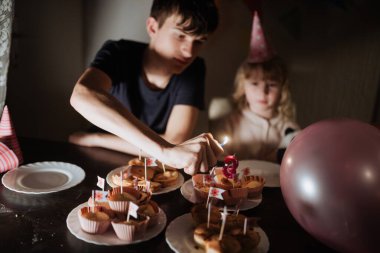 İki kardeş, kek mumu yakarken neşeli bir anın tadını çıkarıyorlar. Etrafları renkli süslemelerle çevrili. Memleketteki kutlama için neşeli bir ortam yaratıyorlar..