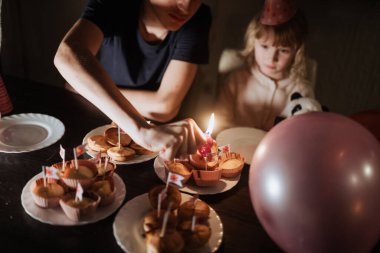 Kardeşler, masada keklerle doğum günü kutlamalarının tadını çıkarırlar. Bir kardeş mum yakarken diğeri heyecanla izliyor. Etrafı şenlikli süslemeler ve balonlarla çevrili..