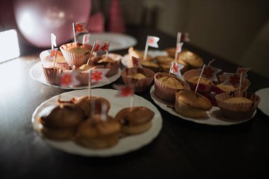 Her biri küçük dekoratif bayraklarla süslenmiş çeşitli ev yapımı ikramlarla dolu bir masa. Sıcak atmosfer neşeye neşe katıyor.