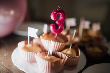 Üçüncü doğum gününü ev yapımı keklerle kutluyoruz. Üç numaralı pembe mum ve dekoratif bayraklarla süslenmiş.