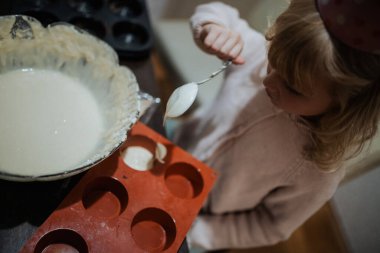 Küçük kız sıcak bir mutfakta kaşıkla hamur topluyor.. 