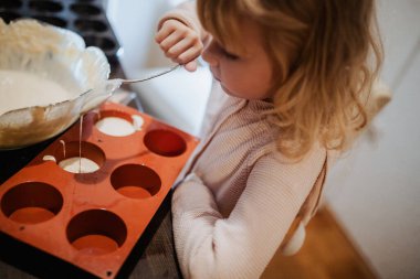 Küçük bir çocuk mutfakta yemek pişirmekten zevk alır, hamuru dikkatlice kırmızı kek tepsisine koyar. Sıcak atmosfer, eğlenceli ve yaratıcı bir aktivite sırasında kardeş ilişkisinin altını çiziyor.