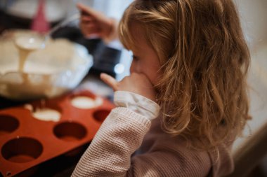 Genç bir kız mutfakta oturur, silikon bir kalıba hamur dökmeye odaklanır.. 