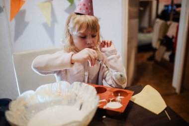 Parti şapkası takan küçük bir çocuk kaşıkla pişirme tepsisine vuruyor..