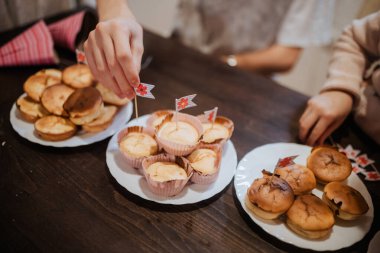 İki kardeş bir aile toplantısında küçük bayraklarla süslenmiş lezzetli ev yapımı pastaları paylaşıyorlar. Konforlu mutfak ortamları birbirlerine bağlanmaları için sıcak bir ortam yaratıyor..