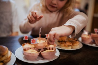 Genç bir çocuk aile toplantısında renkli bayraklı bir keke uzanıyor. Kardeşler sıcak ve davetkar bir ortamda kutlama yaparken ikramlardan hoşlanırlar..