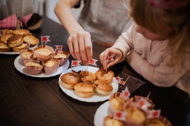 İki kardeş, aile toplantısı sırasında küçük pişmiş yiyecekleri bayrak ile süslemekten hoşlanırlar. Neşeli atmosfer bağlarını ve paylaştıkları anları vurgular..