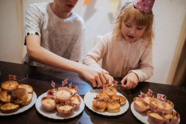 İki kardeş bir aile toplantısında lezzetli kekleri süslerken neşeli bir anın tadını çıkarıyorlar. Neşeli atmosfer birbirine karşı heyecan ve sevgiyle dolu..
