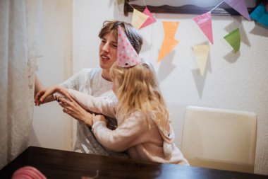 İki kardeş evde doğum günü kutlarken neşeli bir anı paylaşıyorlar. Renkli dekorasyonlar neşeli etkileşimlere girdikçe neşeli atmosfere eklenir.