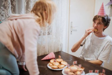 İki kardeş, küçük bir doğum günü partisinde eğlenceli bir anın tadını çıkarırlar. Bir kardeş kek yerken diğeri neşeli bir merakla etrafı şenlikli süslemelerle çevrili..