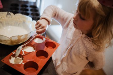 Parti şapkalı küçük bir çocuk, kek tepsisine kaşıkla vurmaya odaklanmış.. 