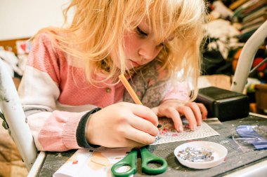 Sarışın kız evde elmas mozaik sanat eserleri yapmaya odaklanmış. Yoğunlaştırılmış ifade, dağınık bir odada siyah bir masanın üzerinde küçük mücevherler ve aletlerle el işi yapmak..